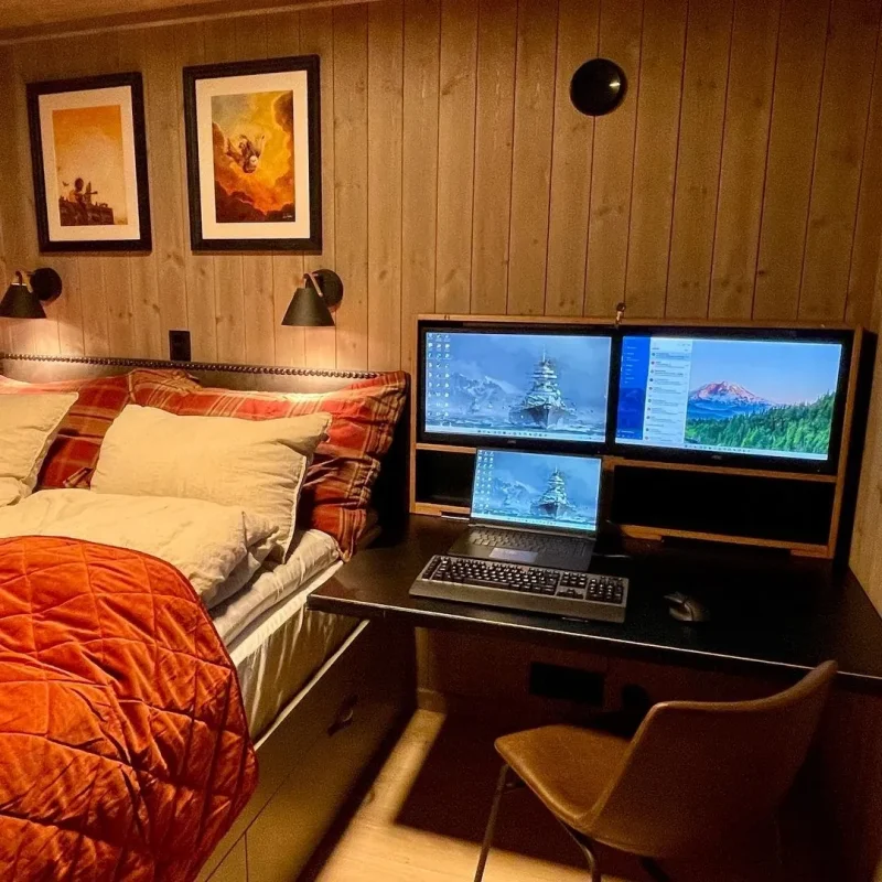 a cozy rustic wooden cabin with a double bed and a large folding desk with two monitors plugged into a laptop and a keyboard and mouse