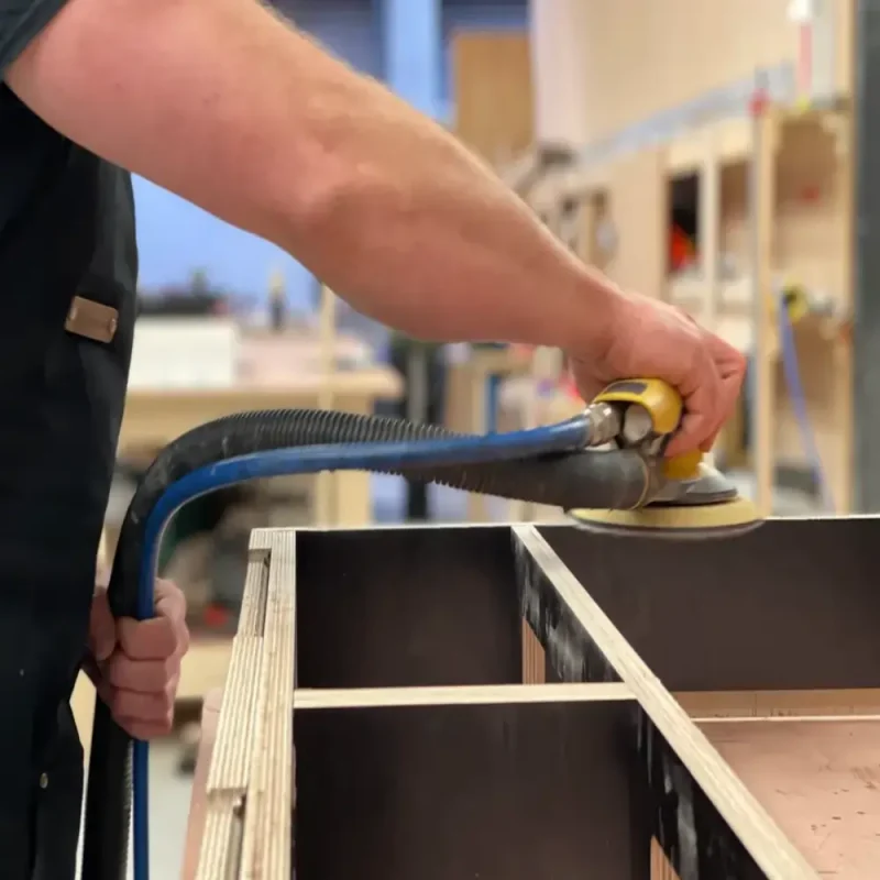 A man building and sanding a fold down desk.