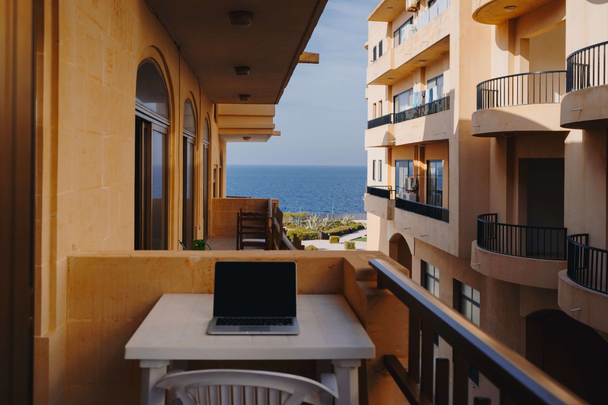 Photo of a laptop on a table on a balcony that overlooks the sea.