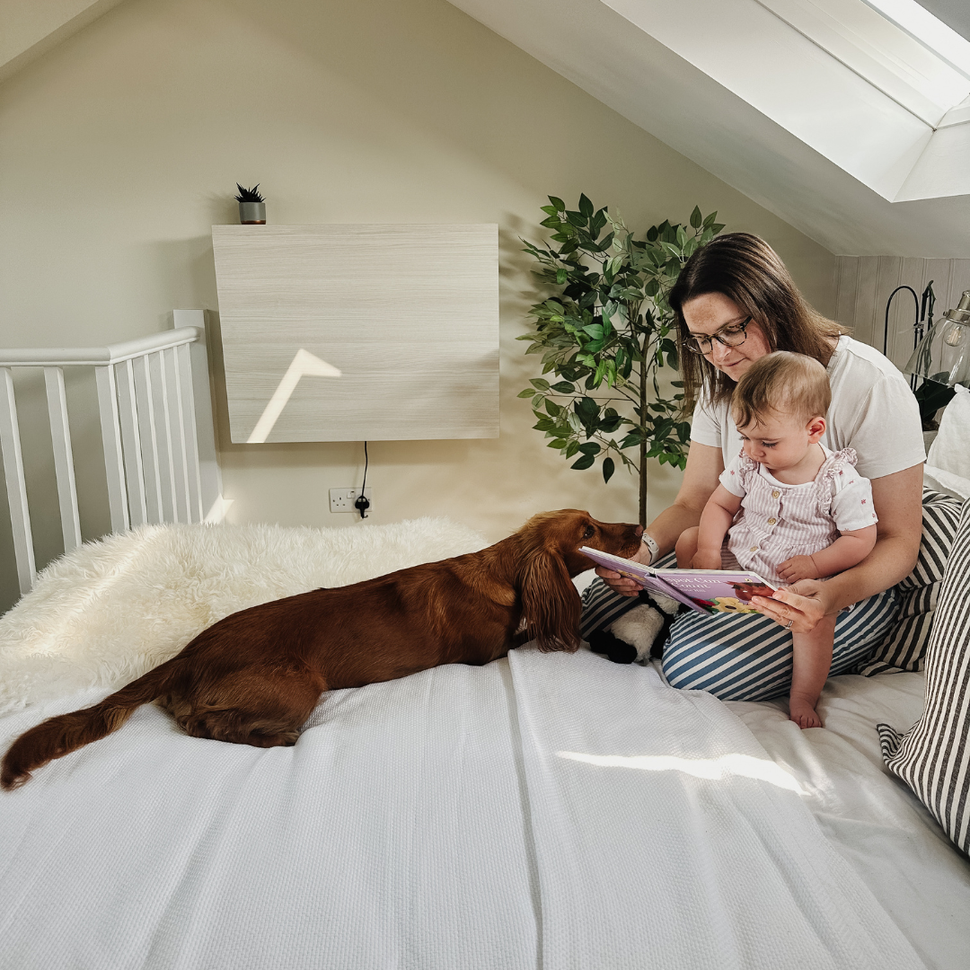 A woman reading a story with her baby and dog with a closed DropTop Desk in the background subtly keeping work out of sight and out of mind